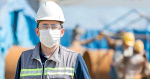 Man wearing safety helmet and mask in front of safety workers